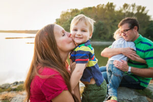 family with two boys smiling sitting by lake