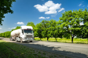 truck driving on road past green trees and fields