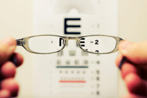 person holding glasses looking at eye doctor test chart