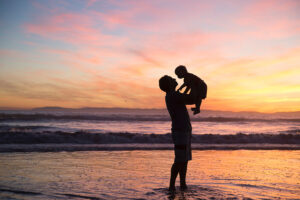 man and baby silhouettes on beach at sunset
