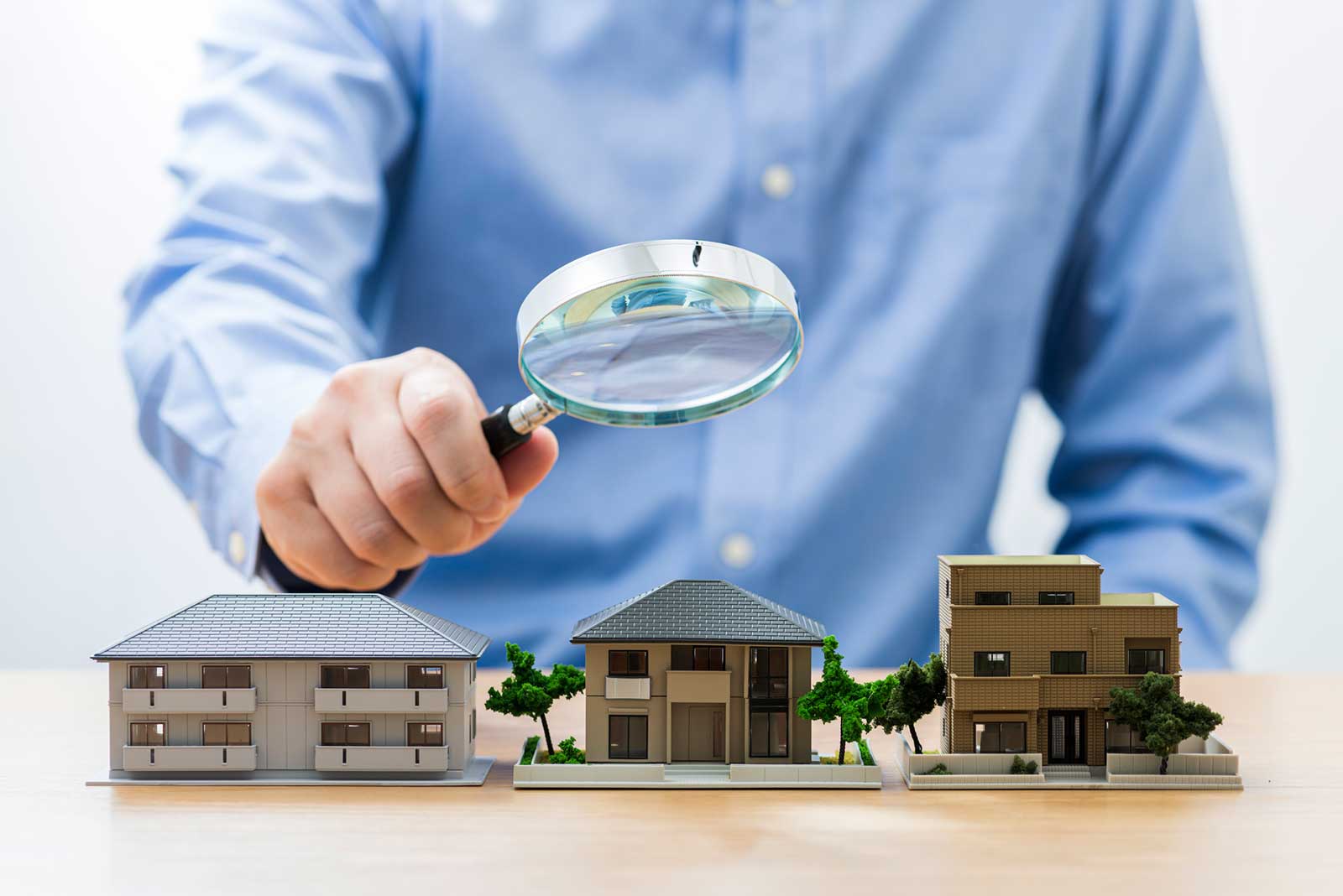 Man holding magnifying glass over model home depicting title search for property 